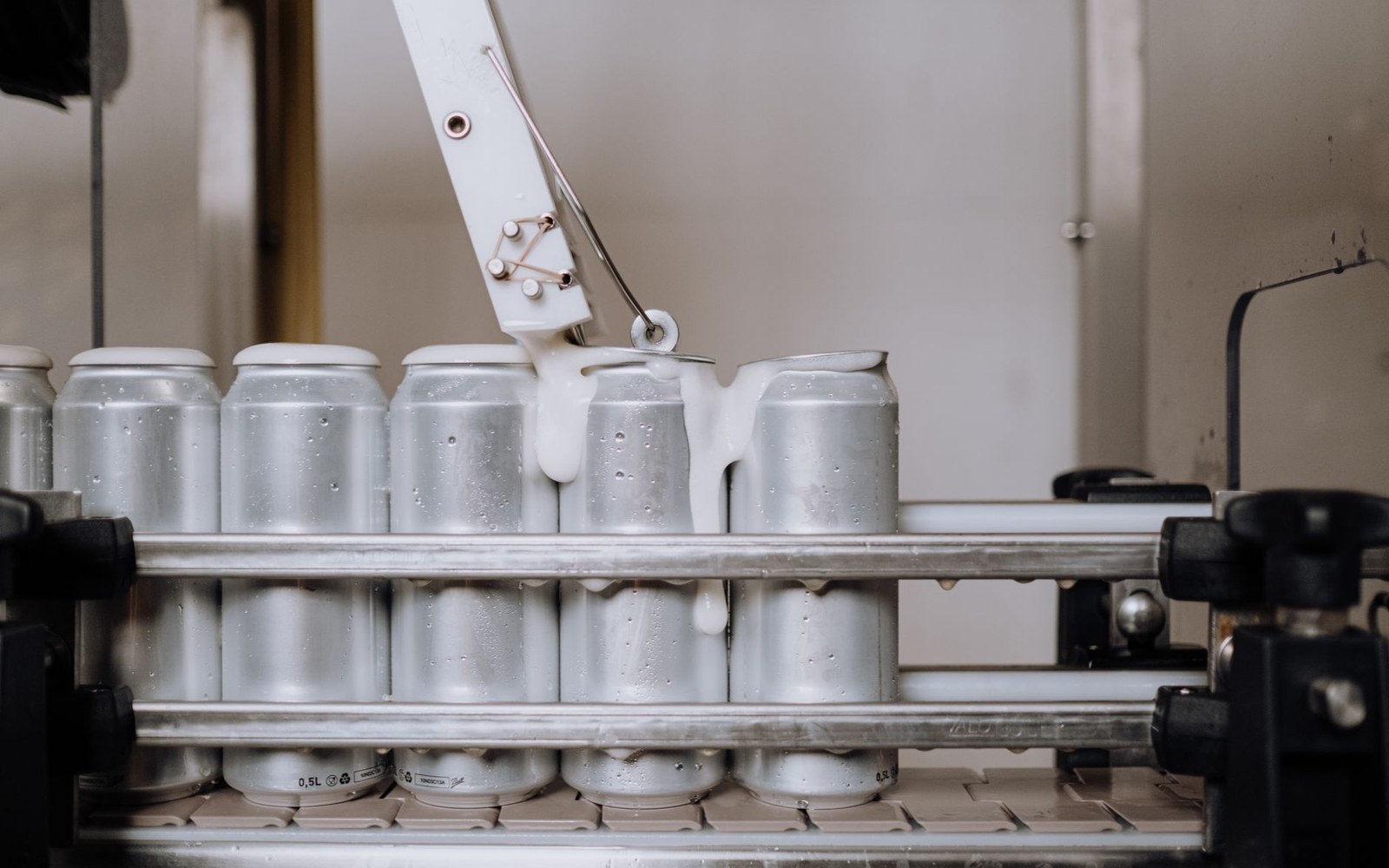 Adult operator at the seamer on a brewery canning line, cans moving under the fill heads, brewery name visible on the wall behind
