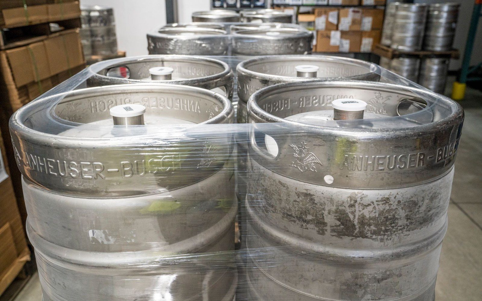 Cold store stacked floor-to-ceiling with branded aluminium kegs, adult worker checking a pallet in the foreground