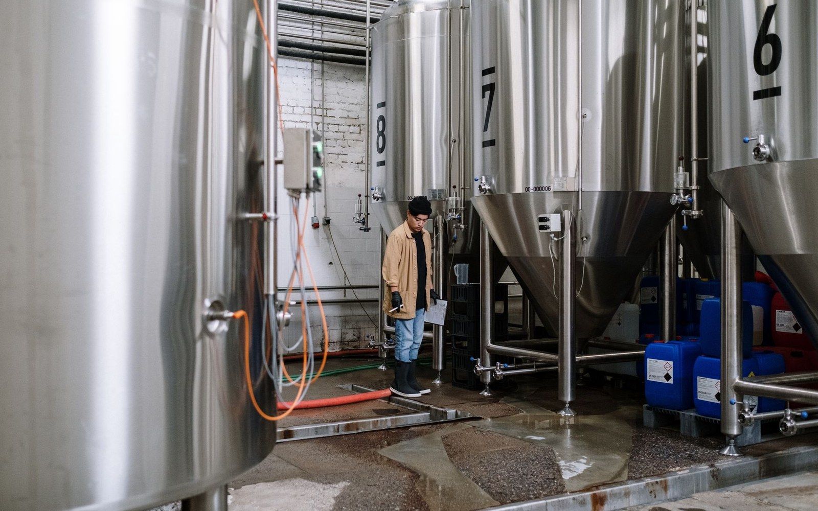 Row of stainless conical fermenters seen from the elevated walkway, a figure visible on the grating at the far end