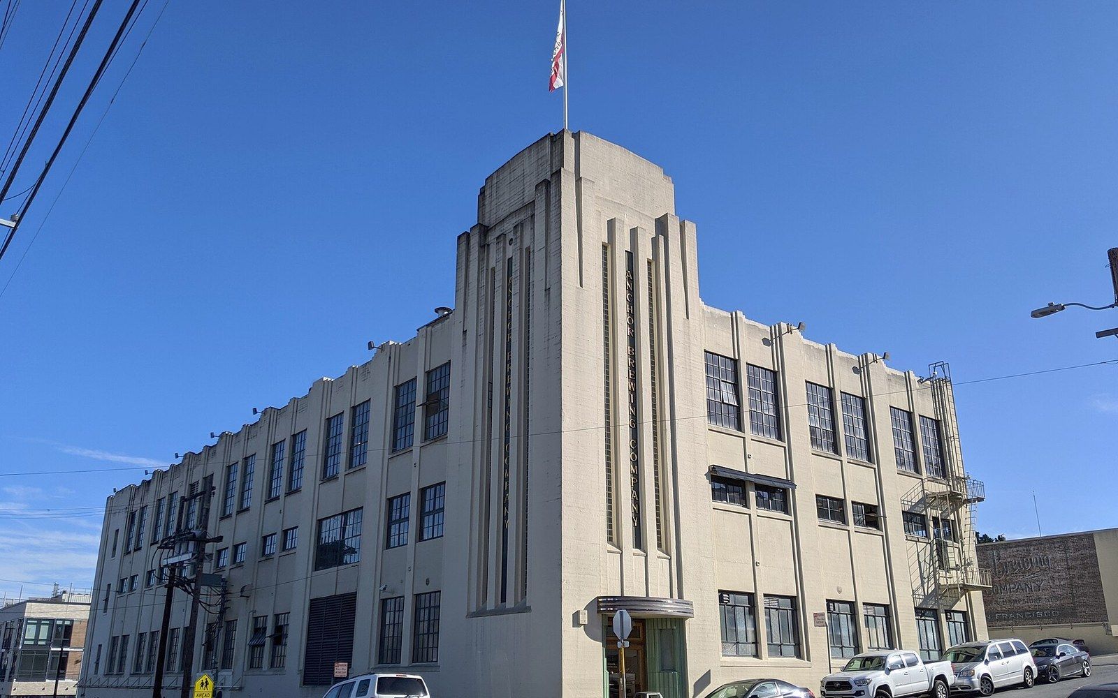 Art deco corner building with a flag atop its stepped central tower under clear sky