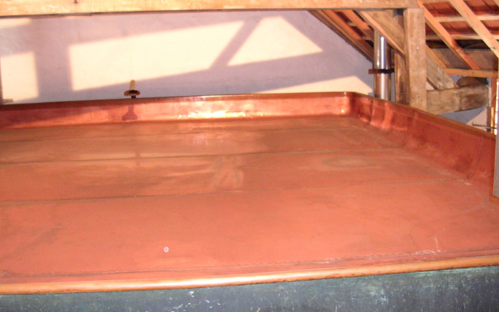 Large flat copper cooling tray sits under wooden roof beams in an attic space