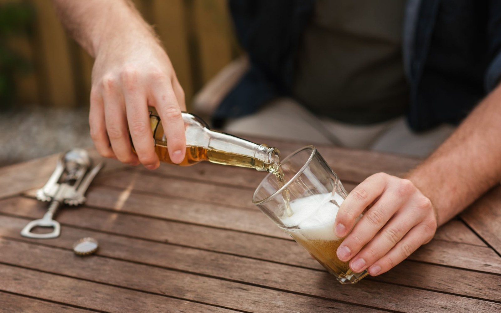 A person pours beer from a bottle into a glass on a wooden table