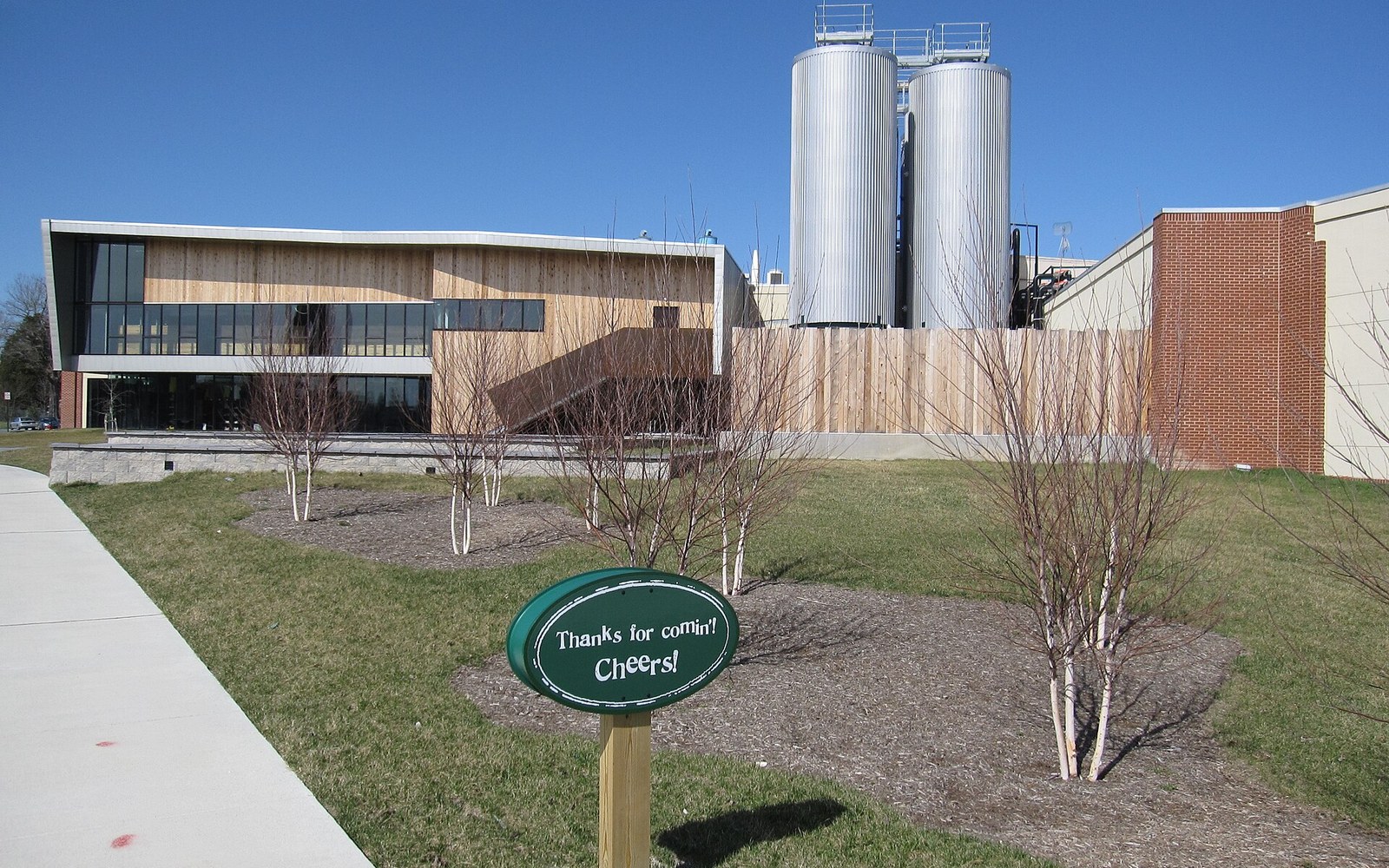 Brewery building with tall storage tanks and a "thanks for comin' cheers" sign