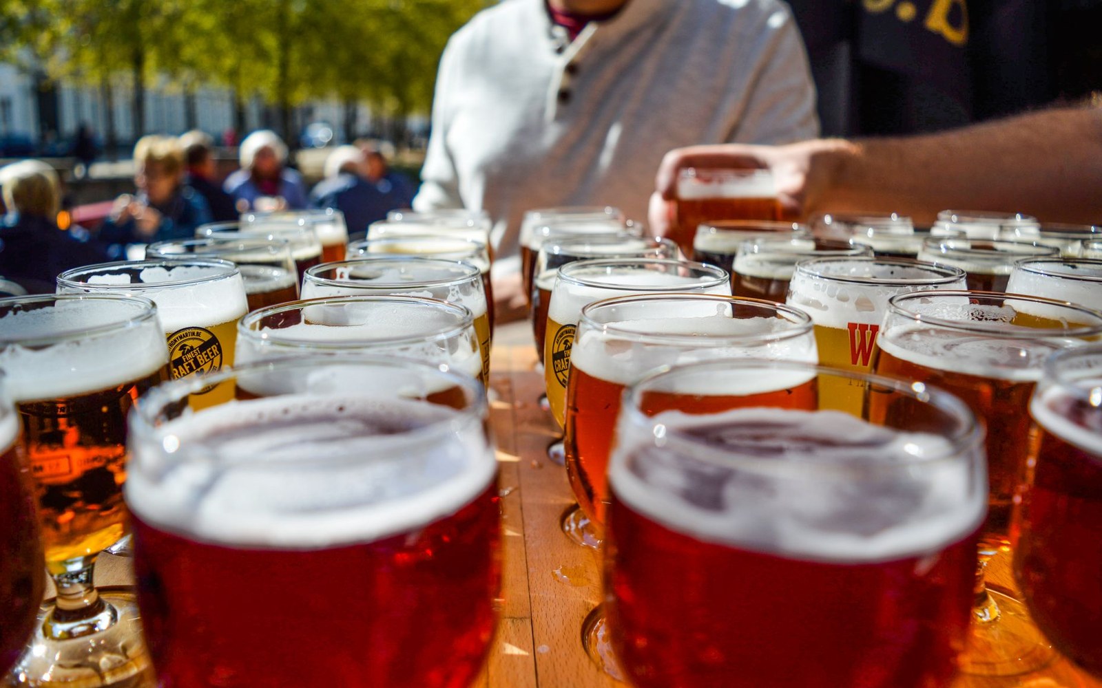 Rows of full beer glasses crowd an outdoor table as a server reaches for one