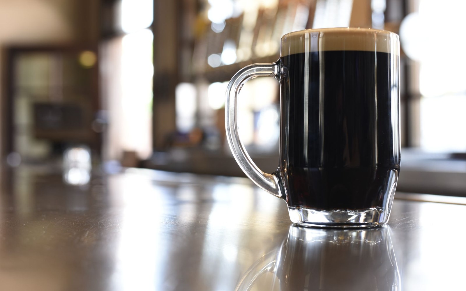A glass mug of dark stout beer with a creamy head sits on a bar counter