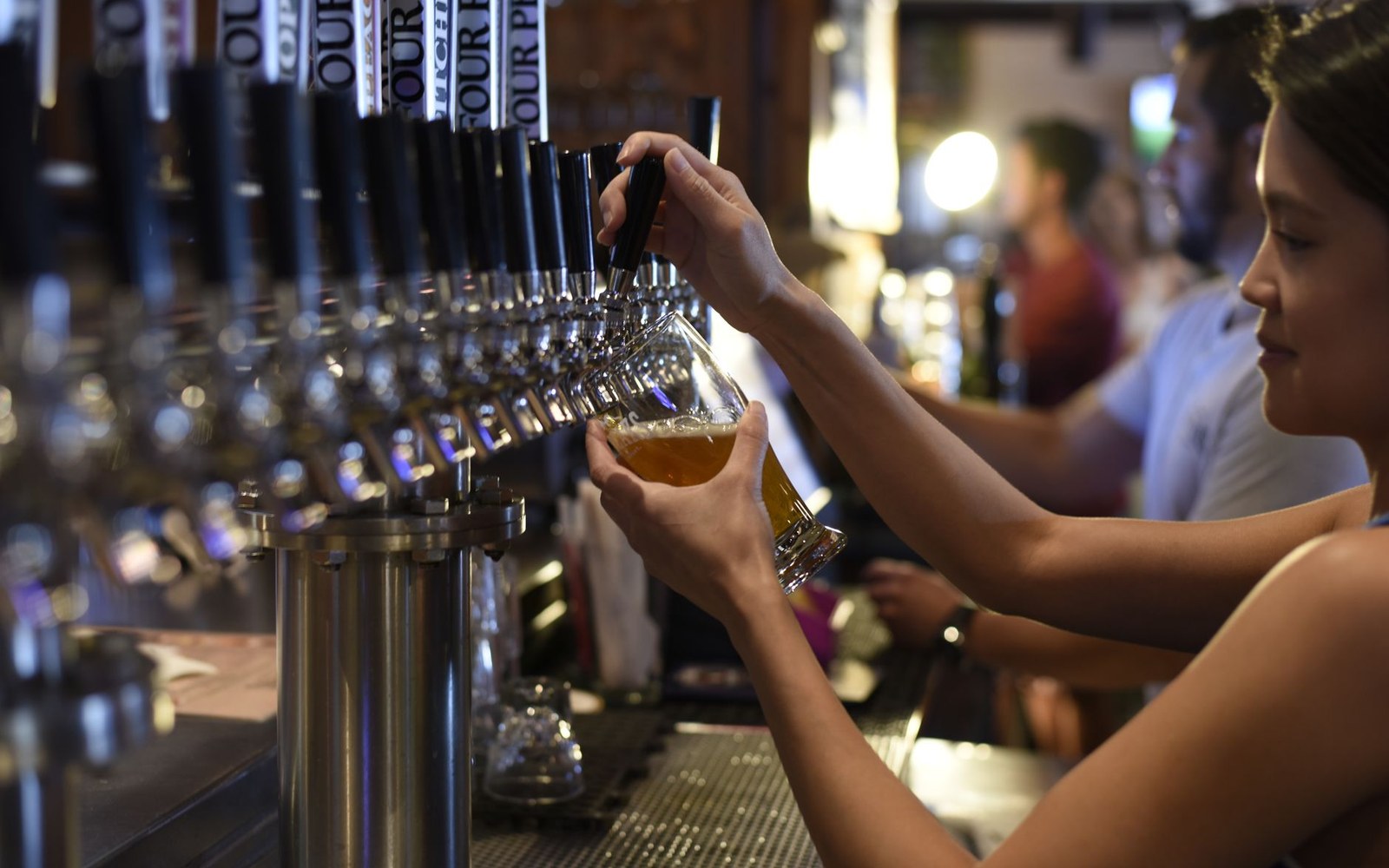 A bartender pours a draft beer from a row of taps into a glass
