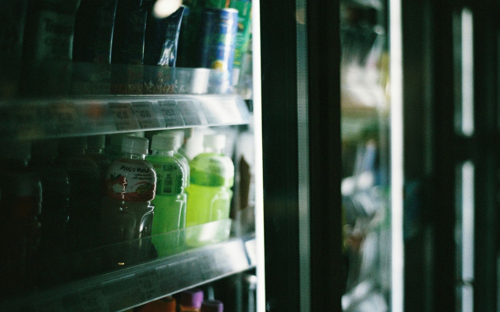 Bottled drinks lined up on shelves inside a glass-door refrigerator case