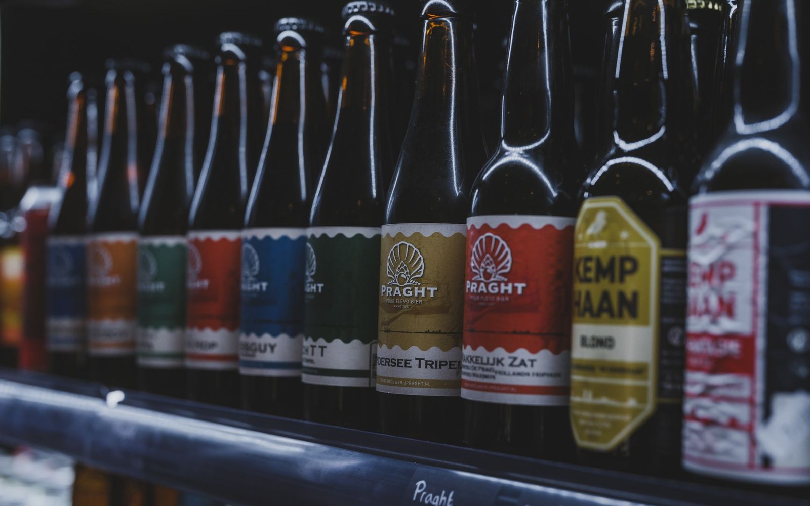 Supermarket beer aisle shot straight on, full-width, named brand packaging visible on the shelves